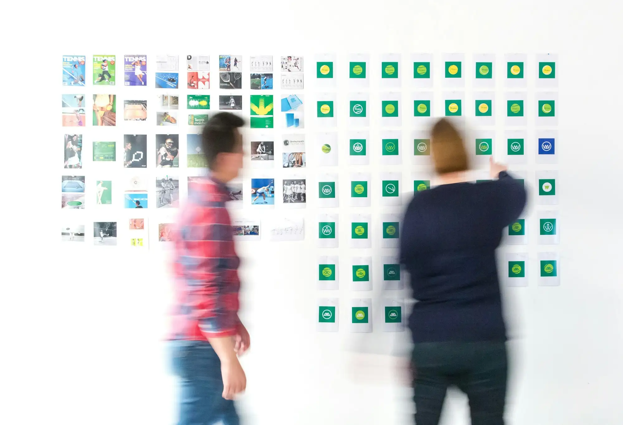 Two people reviewing a wall of printed design work